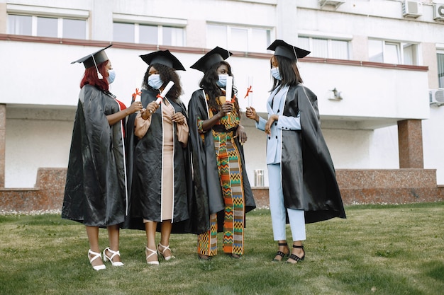 Vier jonge afro-amerikaanse vrouwelijke studenten gekleed in zwarte afstudeerjurk. campus als achtergrond