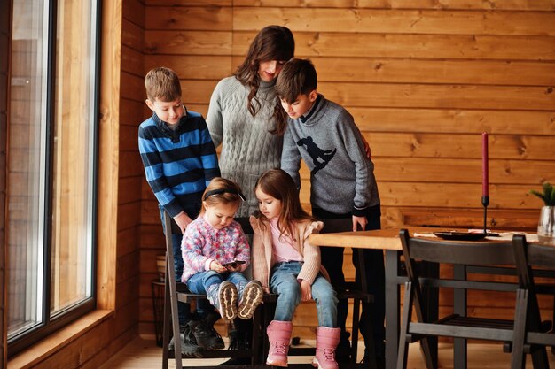 Vier kinderen met moeder in modern houten huis kijken naar video op mobiele telefoon