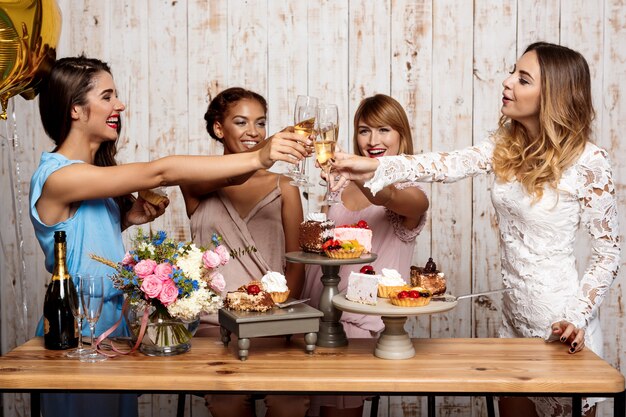 Vier mooie meisjes rammelende glazen met champagne op feestje.