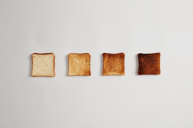 Vier sneetjes brood van geroosterd tot verbrand bereid in een broodrooster in een rij tegen een wit oppervlak. Set toastbroodjes voor het maken van heerlijke knapperige sandwiches. Lekker ontbijt, eten koken