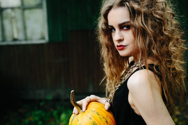 Vintage vrouw als heks, poserend tegen de achtergrond van een verlaten plek aan de vooravond van halloween