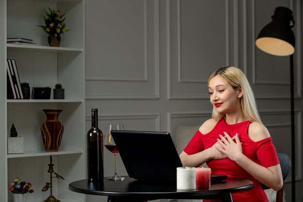 Virtueel liefdes schattig blond meisje in rode jurk op afstandsdatum met wijn op de borst