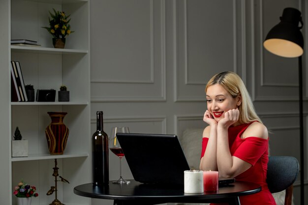 Virtueel liefdes schattig blond meisje in rode jurk op afstandsdatum met wijn opgewonden glimlachend