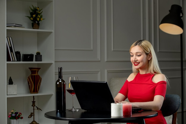 Virtueel liefdes schattig blond meisje in rode jurk op afstandsdatum met wijn typen en lachen