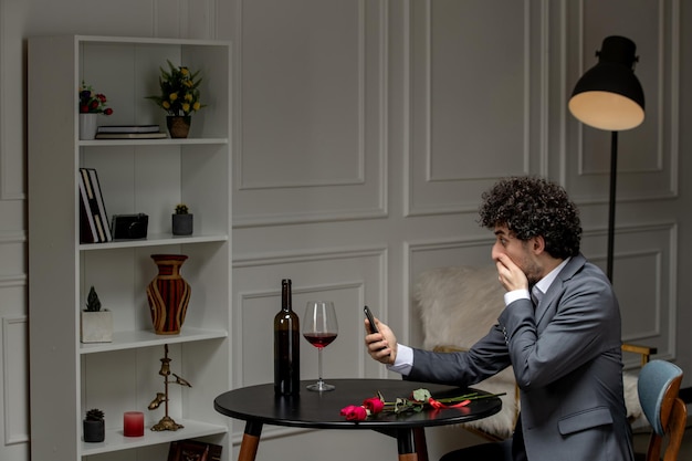 Gratis foto virtuele liefde knappe, schattige kerel in pak met wijn op een telefoondatum op afstand die de mond bedekt