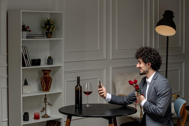 Virtuele liefde knappe schattige kerel in pak met wijn op een telefoondatum op afstand met bloemen