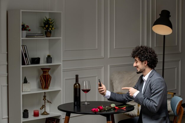 Virtuele liefde knappe schattige kerel in pak met wijn op een telefoondatum op afstand wijzend op het scherm
