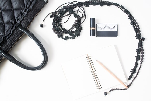 Vlakke lege notitieblok, potlood en vrouwelijke accessoires in zwart concept, bovenaanzicht, geïsoleerd op een witte achtergrond