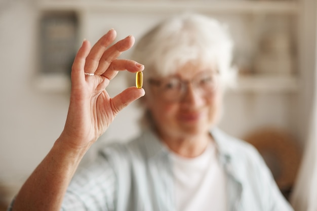 Voedsel, voeding, dieet en gezondheidsconcept. Close-up shot van de hand van een oudere vrouw met visolie of omega-3 meervoudig onverzadigd vetzuursupplement in de vorm van een capsule, die tijdens de lunch wordt ingenomen