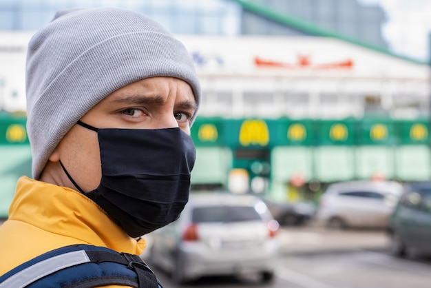 Voedselkoerier met zwart medisch masker op parking. levering van eten