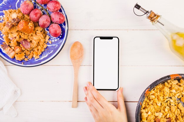 Voedselplaten en hand met mobiele telefoon op kooktafel