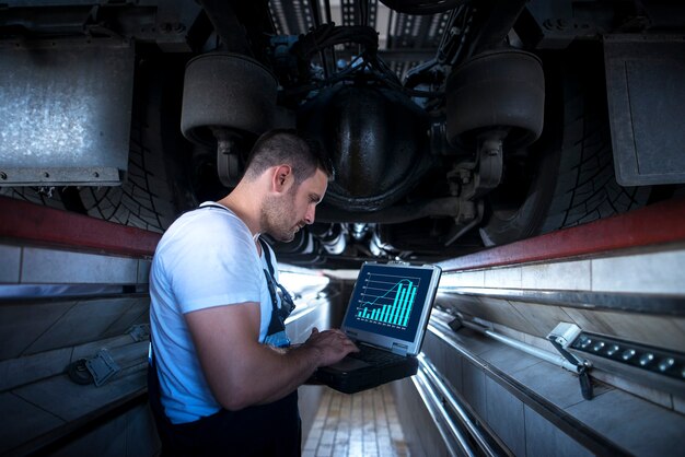 Voertuigmonteur met diagnosetool laptop werkt onder de vrachtwagen in de werkplaats