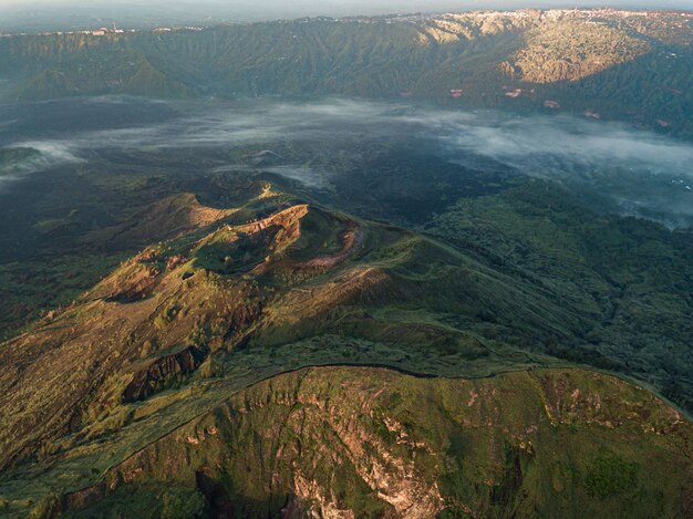 Vogelperspectief van heuvels bedekt met groen en mist onder het zonlicht - perfect voor behang