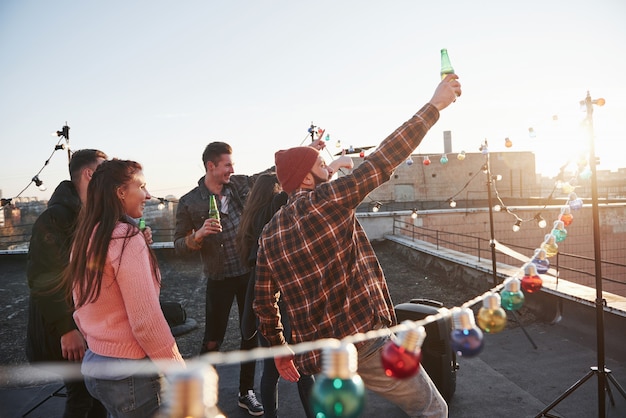 Voldoet aan de dageraad. Vakantie op het dak. Vrolijke groep vrienden staken hun handen omhoog met alcohol