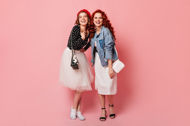 Volle lengte weergave van gelukkige zusters lachen om de camera. Studio shot van trendy meisjes poseren op roze achtergrond met glimlach.