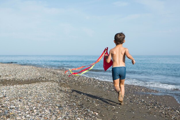 Volledig geschoten kind spelen met vlieger op het strand