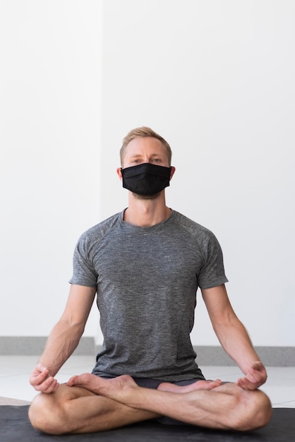 Volledig geschoten man met gezichtsmasker sukhasana pose binnen op de mat