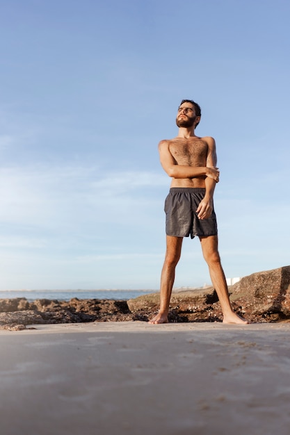 Gratis foto volledig geschoten man met harige borst aan zee