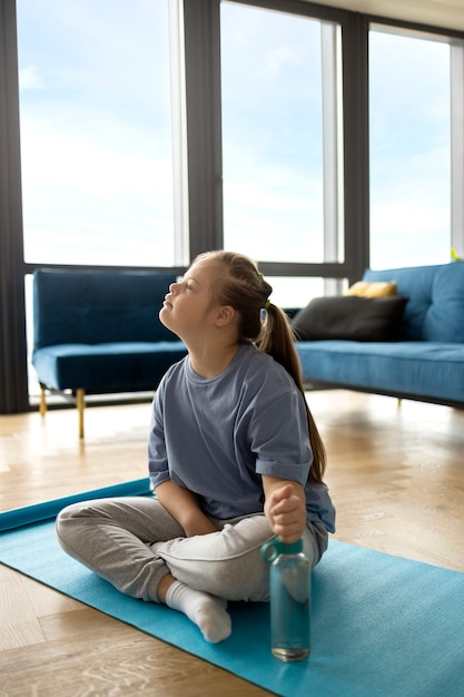 Volledig geschoten meisje zittend op yogamat