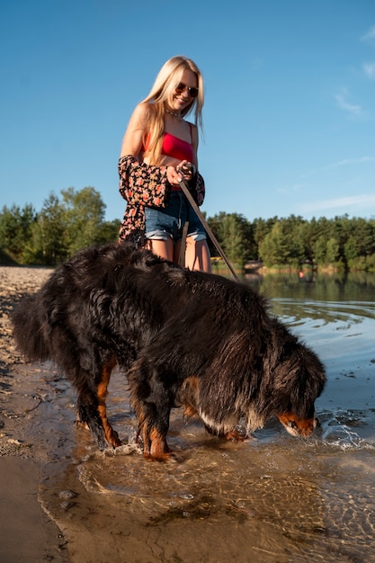 Gratis foto volledig geschoten smileyvrouw met hond bij strand