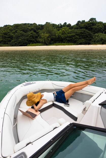 Volledig geschoten vrouw ontspannen op boot met hoed