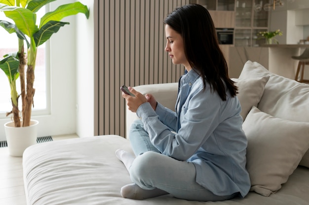 Volledig geschoten vrouw op bank met smartphone