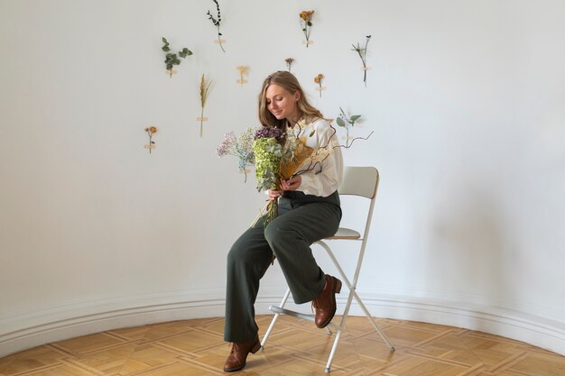 Volledig geschoten vrouw zittend op een stoel met bloemen