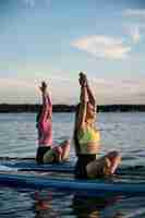 Gratis foto volledig geschoten vrouwen die zich uitstrekken op paddleboard