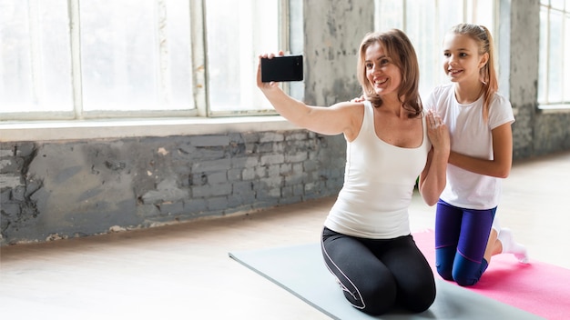 Gratis foto volledig geschotene moeder en dochter die selfie in gymnastiek nemen