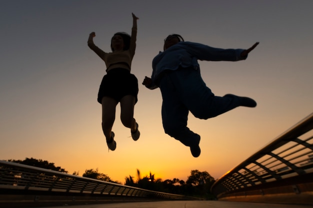 Volledig geschotene vriendensilhouetten die bij zonsondergang springen