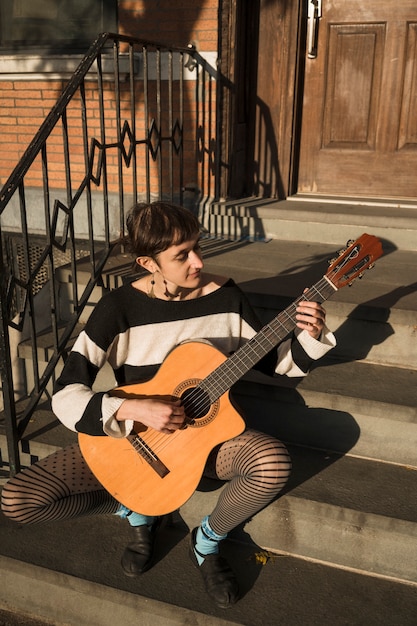 Volledig geschotene vrouw die buitenshuis gitaar speelt