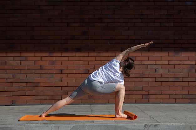 Gratis foto volledig geschotene vrouw die yoga in openlucht op mat doet