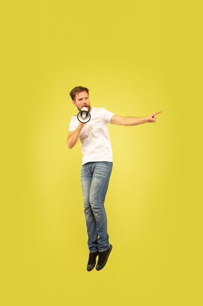 Volledig lengteportret van gelukkige springende mens die op gele achtergrond wordt geïsoleerd. Kaukasisch mannelijk model in vrijetijdskleding