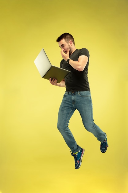Volledig lengteportret van gelukkige springende mens met gadgets die op gele achtergrond worden geïsoleerd