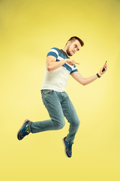 Volledig lengteportret van gelukkige springende mens met gadgets op geel