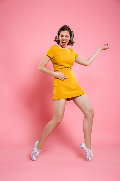 Volledig lengteportret van grappige mooie vrouw in gele kleding die pret heeft terwijl het spelen van luchtgitaar