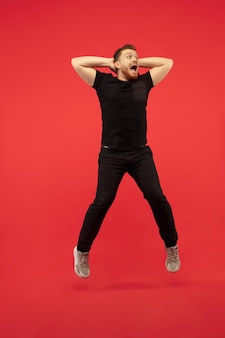 Volledig lengteportret van jonge succesvolle hoogspringende man gebaren geïsoleerd op rode studio