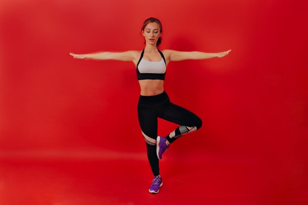 Volledig portret van een fitte vrouw met donker haar, gekleed in een sportuniform, maakt yogabewegingen