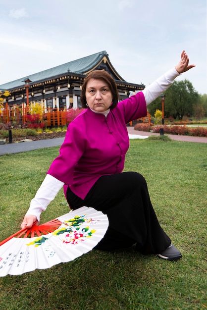 Gratis foto volledig shot vrouw die tai chi beoefent met fan