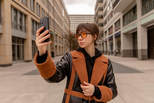 Volledig zicht op de vrouw op straat, kijk naar de telefoon met een oranje zonnebril