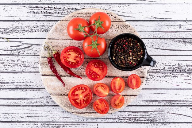 Volledige en halve tomaten op wit bord droge roodgloeiende chili peper geïsoleerd en zwarte peper poeder in zwarte kom op witte houten oppervlak