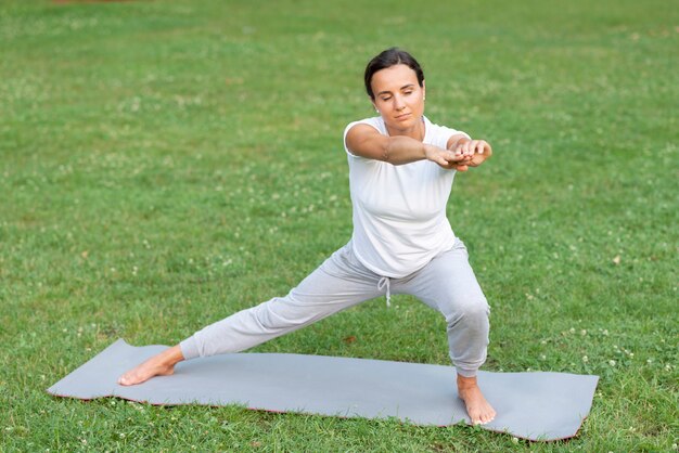 Volledige geschotene vrouw die yoga in aard doet