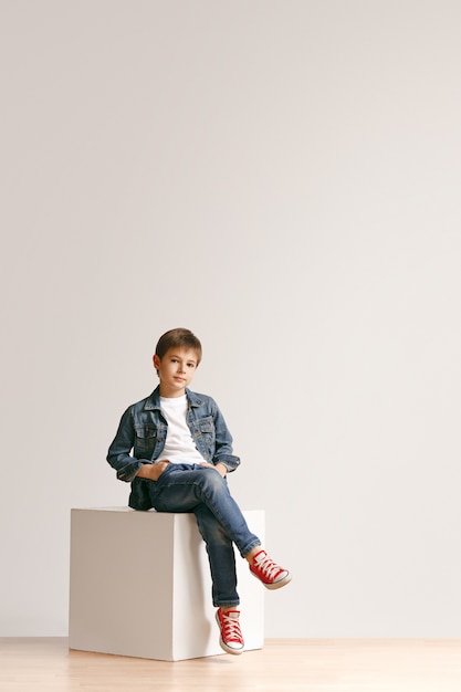 Volledige lengte portret van schattige kleine jongen jongen in stijlvolle jeans kleding en glimlachen, staande op wit. Kindermode concept