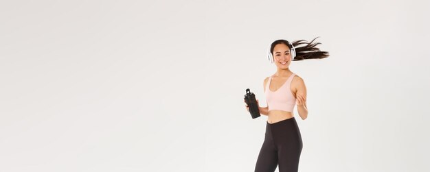 Volledige lengte van een glimlachend, aantrekkelijk aziatisch vrouwelijk athelte-meisje dat fitnesstraining doet in de sportvrouw van de sportschool