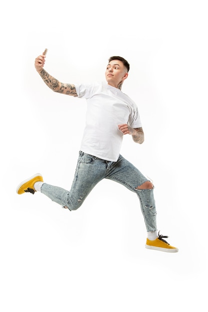 Volledige lengte van knappe jonge man die telefoon neemt tijdens het springen tegen oranje studioachtergrond. Mobiel, beweging, beweging, bedrijfsconcepten