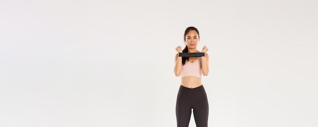 Volledige lengte van lachende en vastberaden slanke brunette Aziatische fitnessmeisje trainingscoach die oefening toont