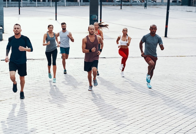 Volledige lengte van mensen in sportkleding die joggen terwijl ze buiten op het trottoir trainen