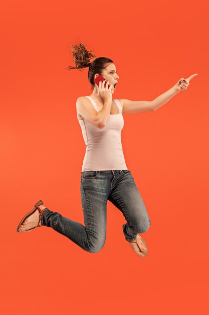 Volledige lengte van vrij jonge vrouw met mobiele telefoon tijdens het springen