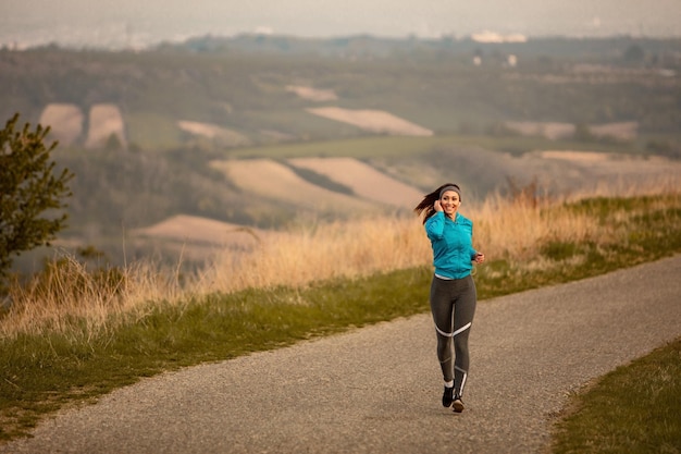 Volledige lengte van vrouwelijke hardloper die muziek luistert tijdens het joggen op de weg bij zonsopgang