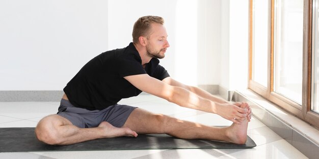 Volledige shot jonge man die zich uitstrekt op yoga mat